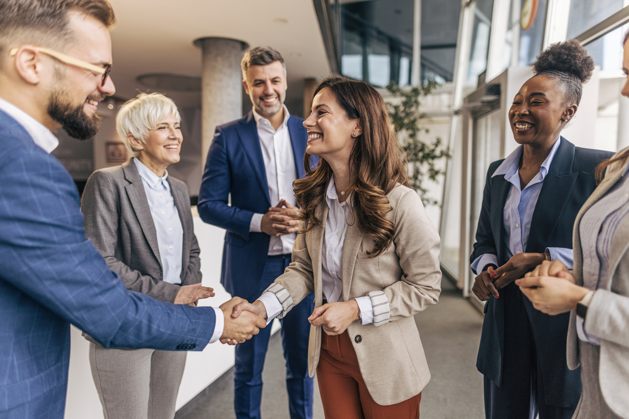 Diverse business team shaking hands and smiling in a bright office lobby.